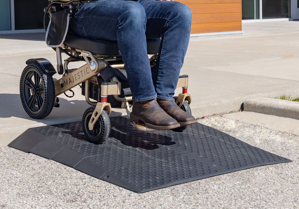 man riding electric ComfyGo wheelchair down a rubber threshold ramp outside a building